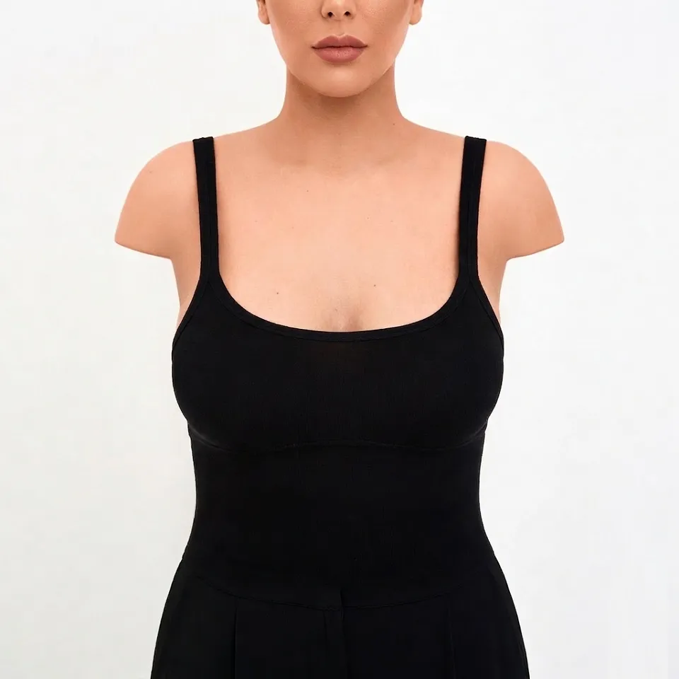 The post operative clinical photograph of the same woman from Image 1, displaying a symmetrically reduced, uplifted, and proportional breast contour following successful Elite Breast Reduction surgery managed by Dina Elite for GCC clients  She wears the identical black ribbed outfit, maintaining the same central pose on a plain white background, highlighting refined contours 