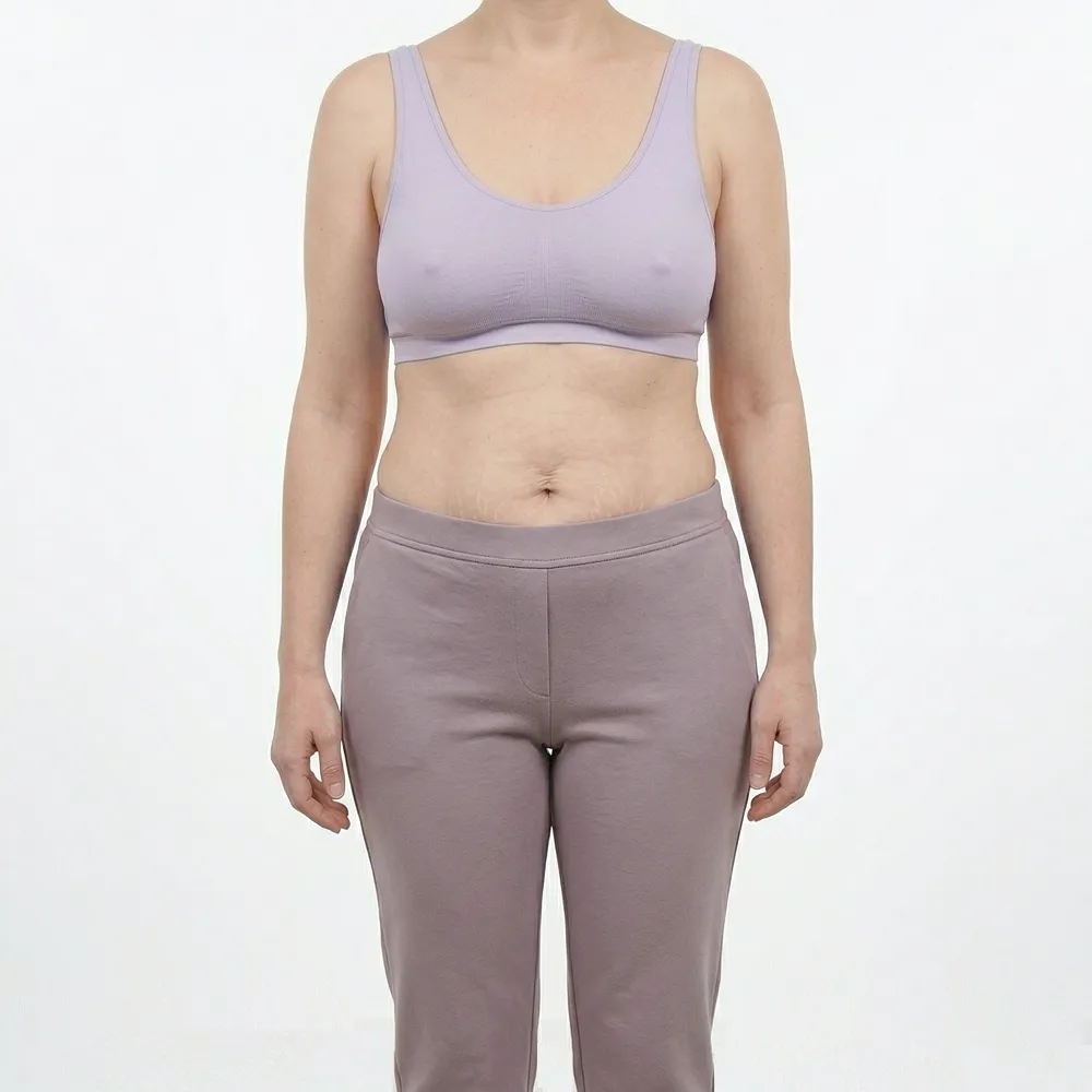 Headless clinical before photograph of a white woman exhibiting post pregnancy abdominal skin laxity, stretch marks, and breast ptosis prior to a comprehensive Mommy Makeover at Dina Elite, targeting patients from the Gulf  She is wearing a soft pink athletic outfit 