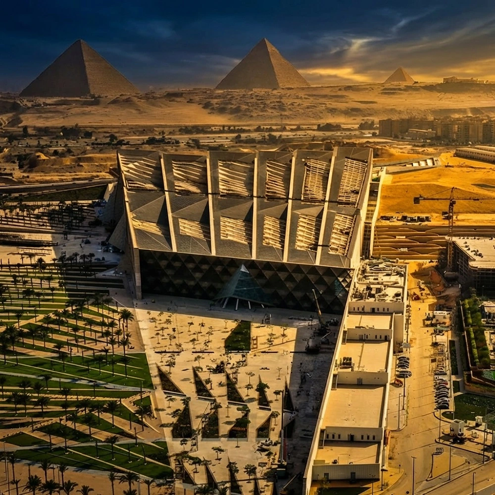 Aerial view of the Grand Egyptian Museum (GEM) at the Giza Pyramids plateau, a luxury landmark integrated into Dina Elite medical tourism programs for clients from Saudi Arabia, United Arab Emirates, Qatar, Kuwait, Bahrain, Oman, Jordan, Iraq, Lebanon, Libya, Palestine, Yemen, Syria, Sudan, Morocco, Algeria, Tunisia, Mauritania, Djibouti, Somalia, and Comoros 
